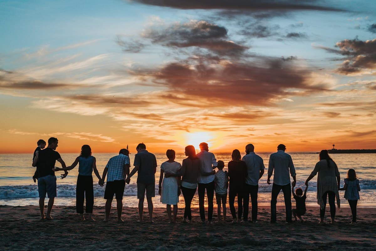 Pessoas de mãos dadas na praia ao pôr do sol.